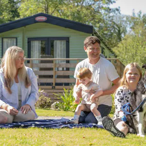 Holiday homeowners at Newby Bridge Country Caravan Park sitting outside on the grass in front of a holiday home.
